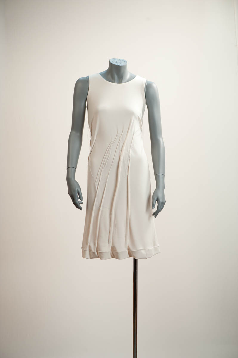 Robe moulée sur le corps. Les plis pincés cousus logent dans les parties creuses du corps. Ces plis ajustent la robe au corps. Ces plis allongés à la verticale et à l’oblique traduisent le mouvement du vent.  Couleur: noir, ivoire, et d’après les couleurs du marché / A dress that molds the body. Sewn, flattened tucks are placed in the hollows of the body.   These vertical and diagonal creases evoke a blowing wind. Colour: black, ivory; other colours as available