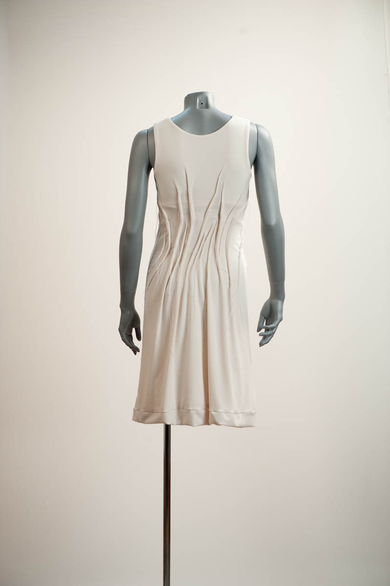 Robe moulée sur le corps. Les plis pincés cousus logent dans les parties creuses du corps. Ces plis ajustent la robe au corps. Ces plis allongés à la verticale et à l’oblique traduisent le mouvement du vent.  Couleur: noir, ivoire, et d’après les couleurs du marché / A dress that molds the body. Sewn, flattened tucks are placed in the hollows of the body.   These vertical and diagonal creases evoke a blowing wind. Colour: black, ivory; other colours as available