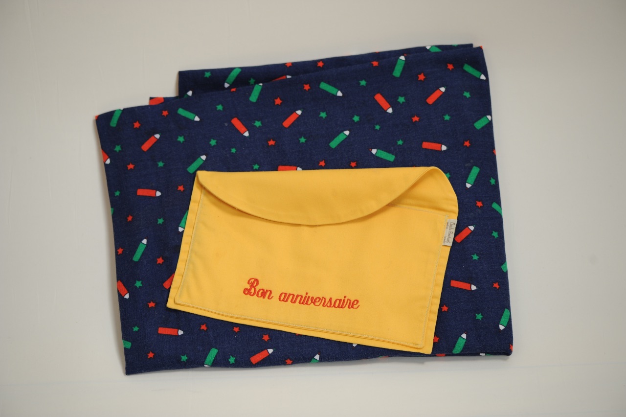 L’inscription Bon Anniversaire est brodé sur l’enveloppe et cousu sur la nappe; pour déposer une carte d’anniversaire.  Couleurs et motifs variés / The envelope with Happy Birthday embroidered on it is sewn onto the tablecloth; to put a birthday card. Varied colours and patterns